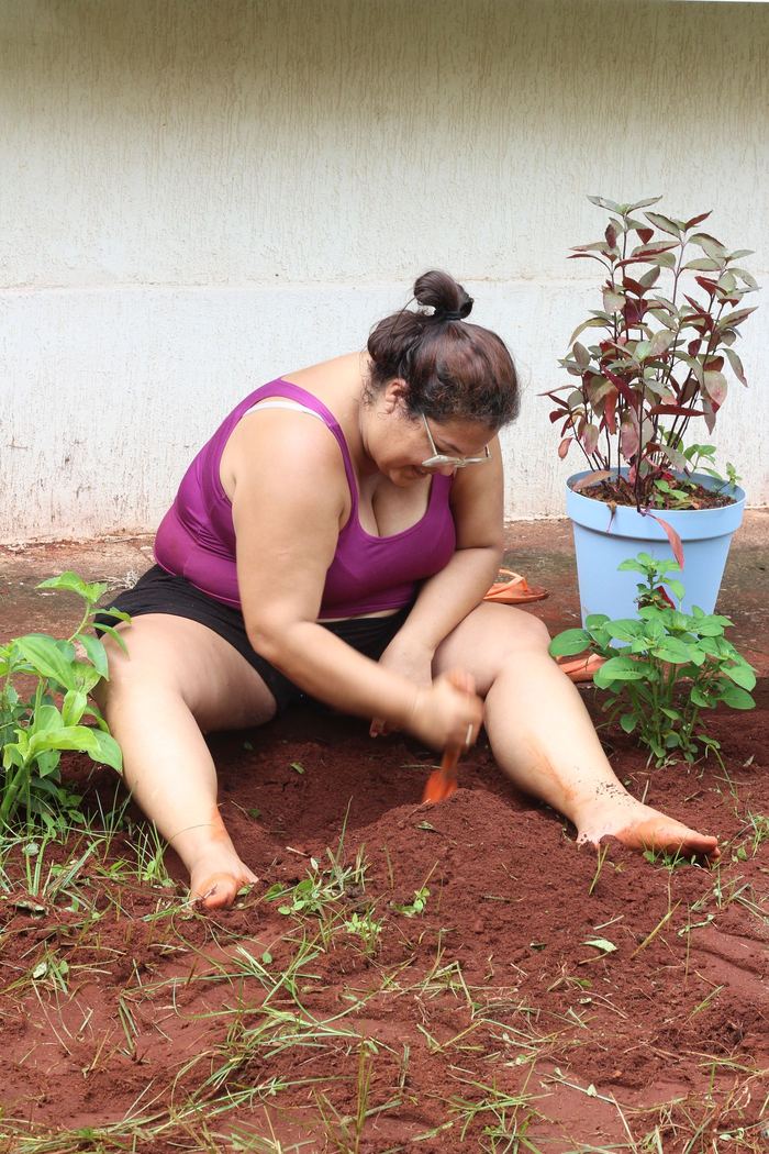 Mulher sentada na terra plantando mudas no canteiro
