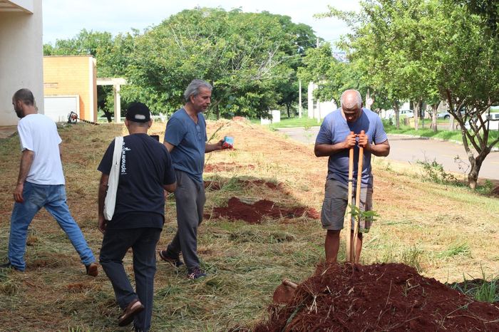 Pessoas preparando o solo com ferramentas ao longo do canteiro
